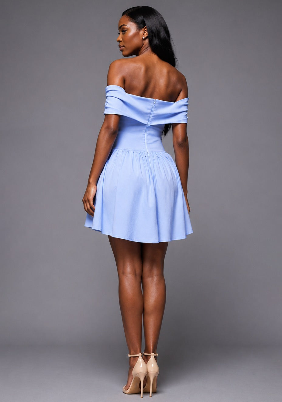 Back image of a model wearing the VSPR Carla Bardot Foldover Blue Mini Dress in Light Blue with a clean off-the-shoulder neckline, tailored body-skimming fit, and contemporary mini-length hem, standing against a grey studio backdrop.