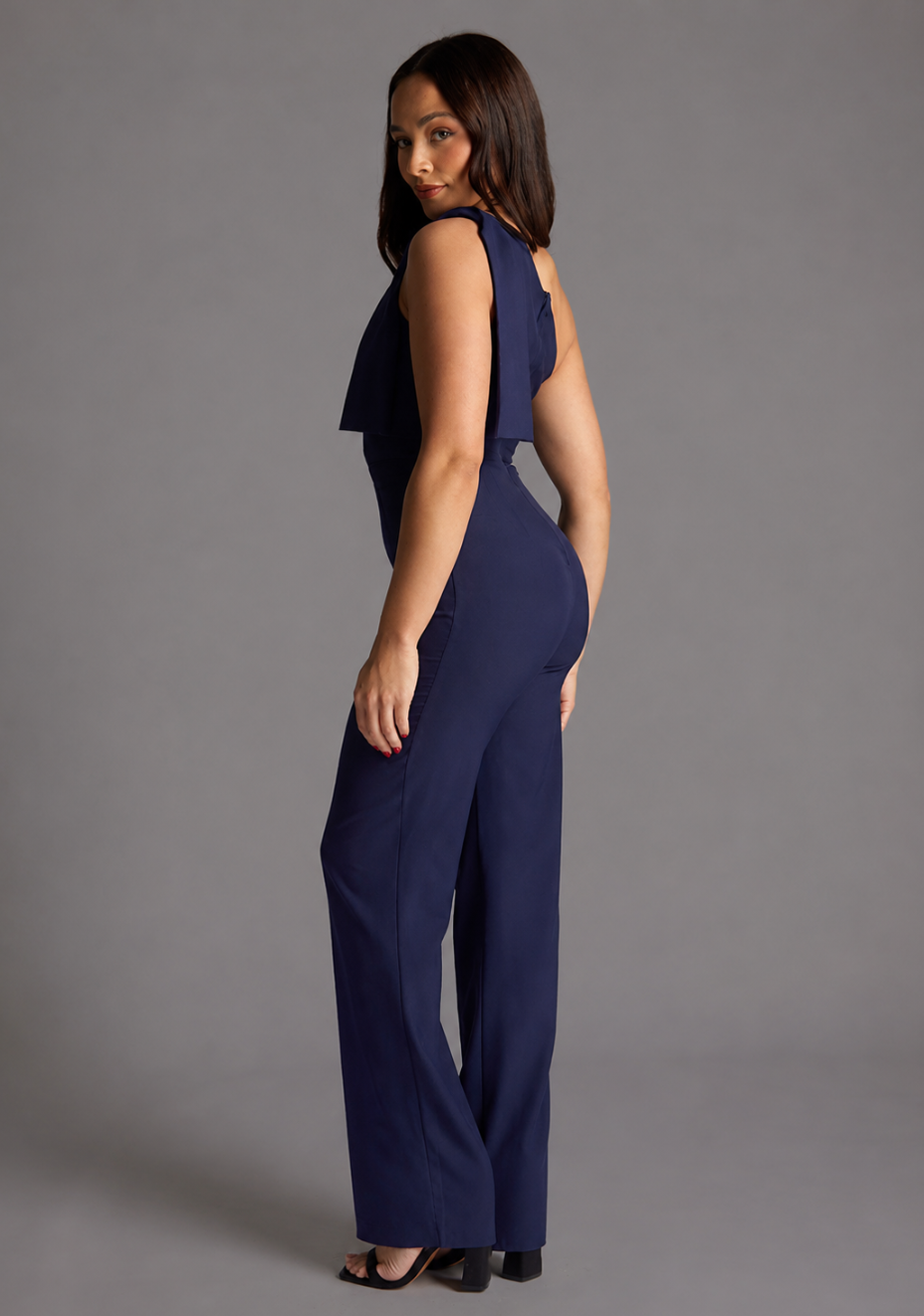Side back image of a model wearing the VSPR Gracie Petite One Shoulder Wide Leg Jumpsuit in Navy, highlighting its clean lines, elegant fit and fluid wide-leg shape.