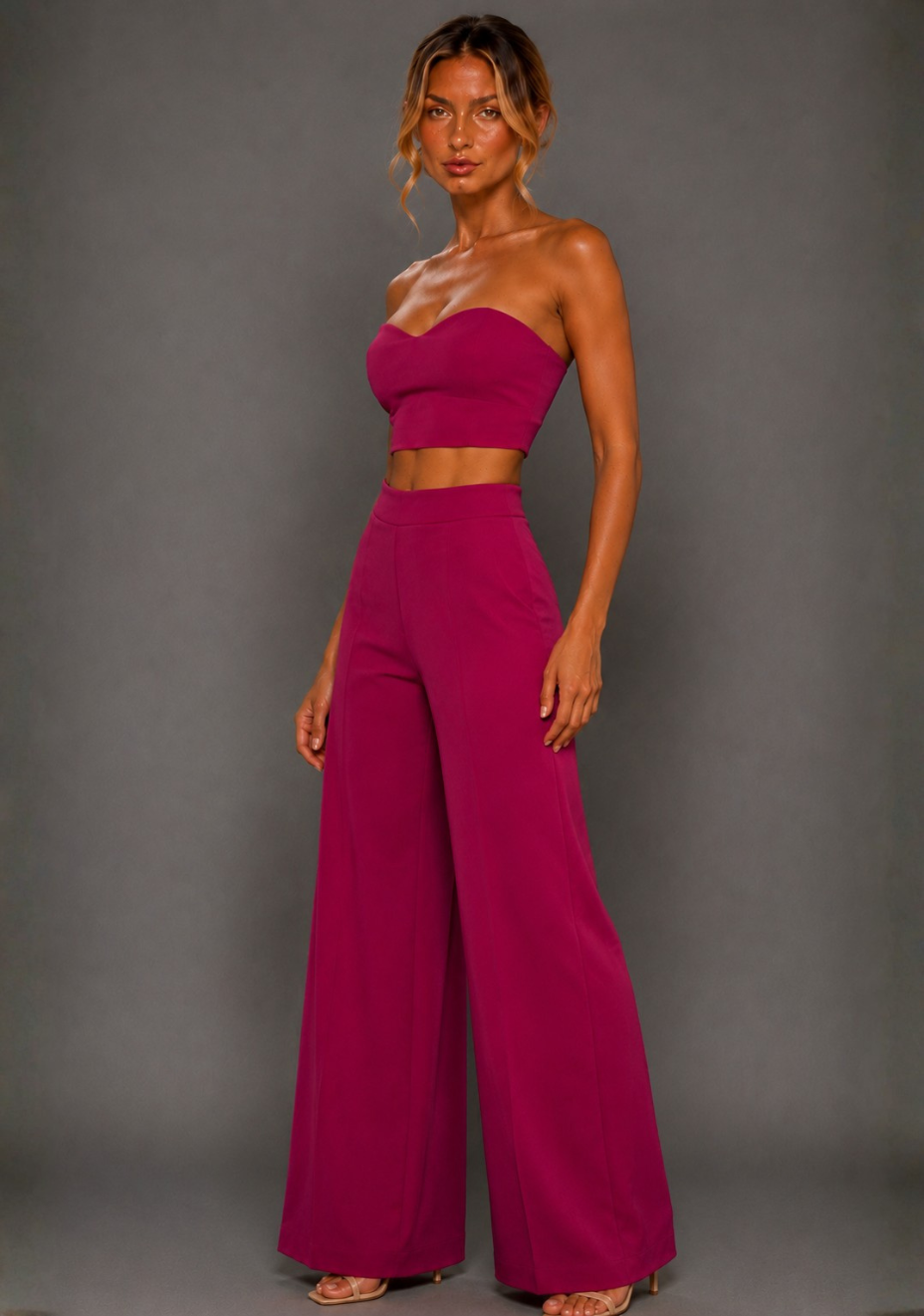 Front image of a model wearing the VSPR Marty Magenta Wide Leg Trousers with a high-rise waist and sweeping wide leg, paired with the matching VSPR Renata Strapless Magenta Crop Top, standing against a grey studio backdrop.