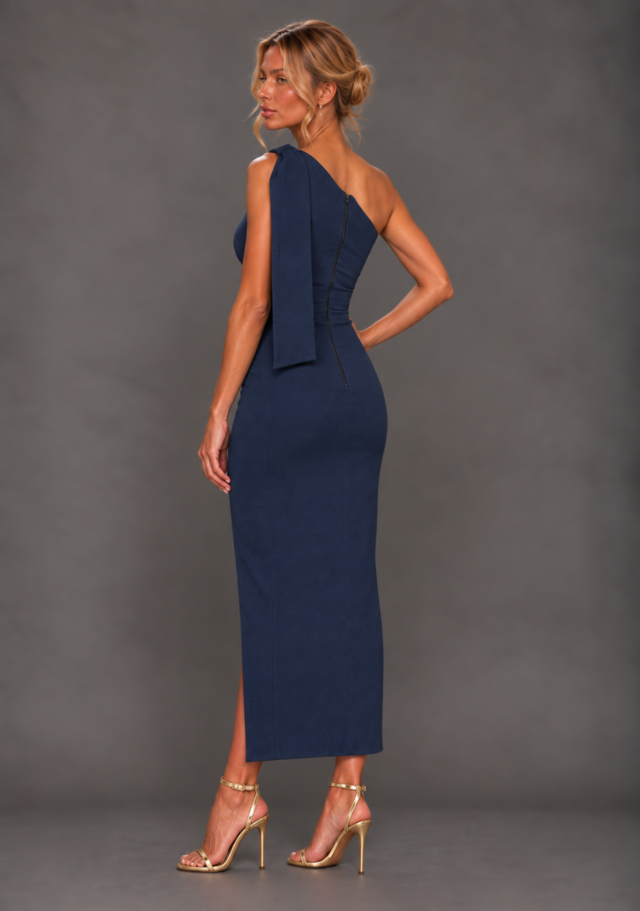 Side back image of a model wearing the VSPR Odette One Shoulder Navy Midaxi Dress, showcasing the sleek fitted silhouette and elegant asymmetric design against a grey studio backdrop.