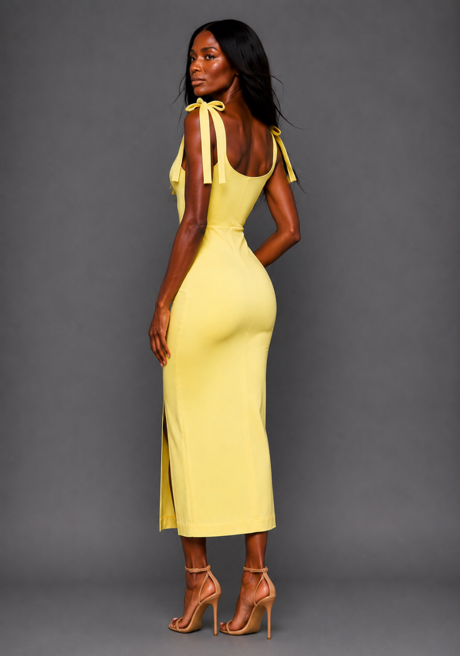 Side back image of a model wearing the VSPR Onyx Square Neck Bow Lemon Midaxi Dress in Lemon, showcasing the sleek figure-skimming shape, delicate shoulder ties, and flowing midaxi skirt against a grey studio backdrop.