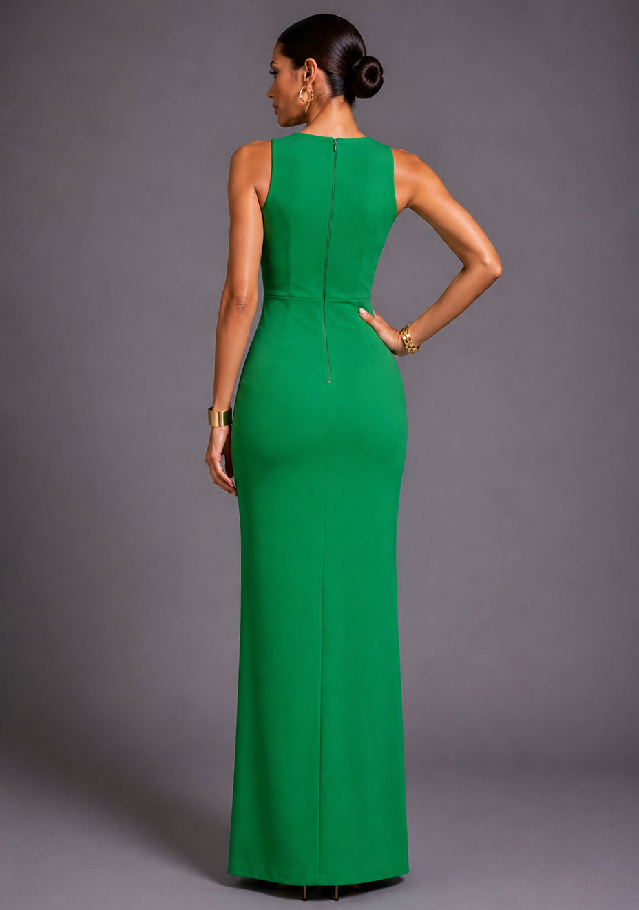 Back image of a model wearing the VSPR Polly Asymmetrical Emerald Green Maxi Dress featuring a clean centre-back zip, streamlined silhouette, and floor-length design, standing against a grey studio backdrop.