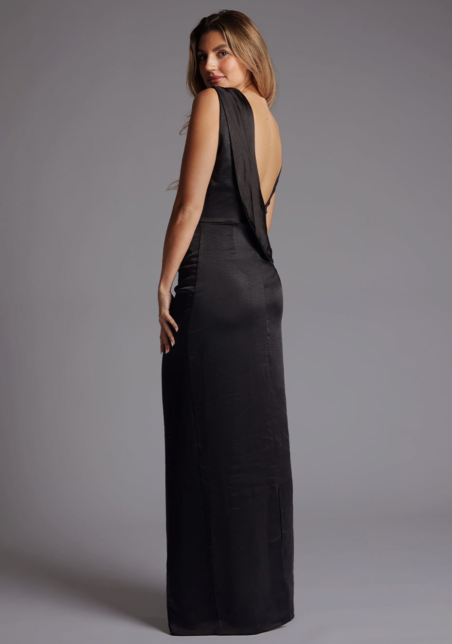 Side back image of a model wearing the Vesper Bertie Open Back Satin Maxi Dress in Black, revealing the dramatic open-back detail and sleek satin finish.