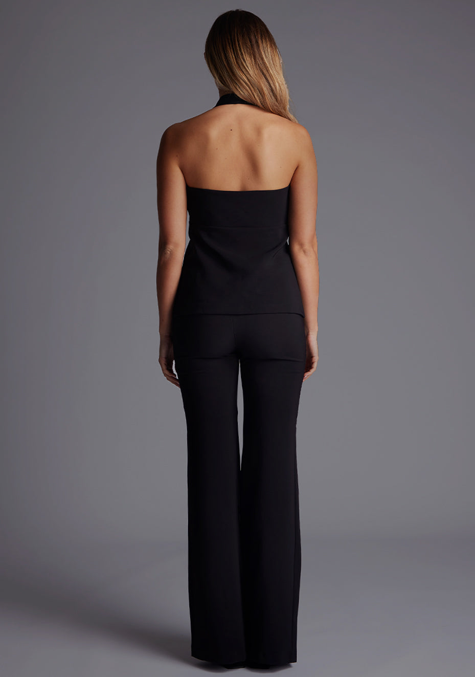 Back image of a model wearing the Vesper Betty Tailored Longline Waistcoat in Black, showcasing the sleek halter-neck back and tailored longline silhouette.