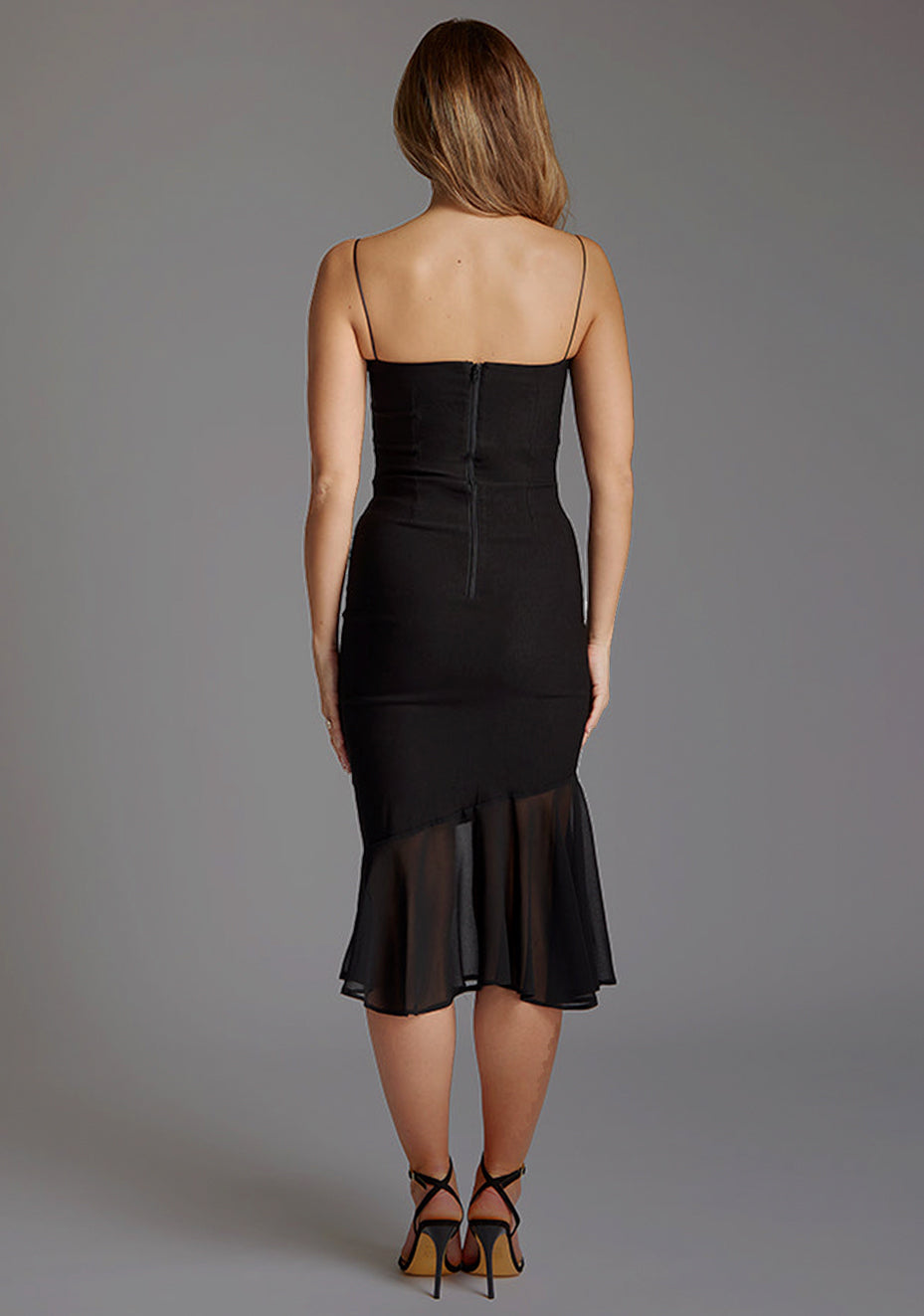 Back image of a model wearing a black frill hem midi dress with a straight neckline with thin straps and a contrast fabric frill hem. The design featured is the Vesper Buffy Frill Hem Square Neckline Midi Dress in Black.