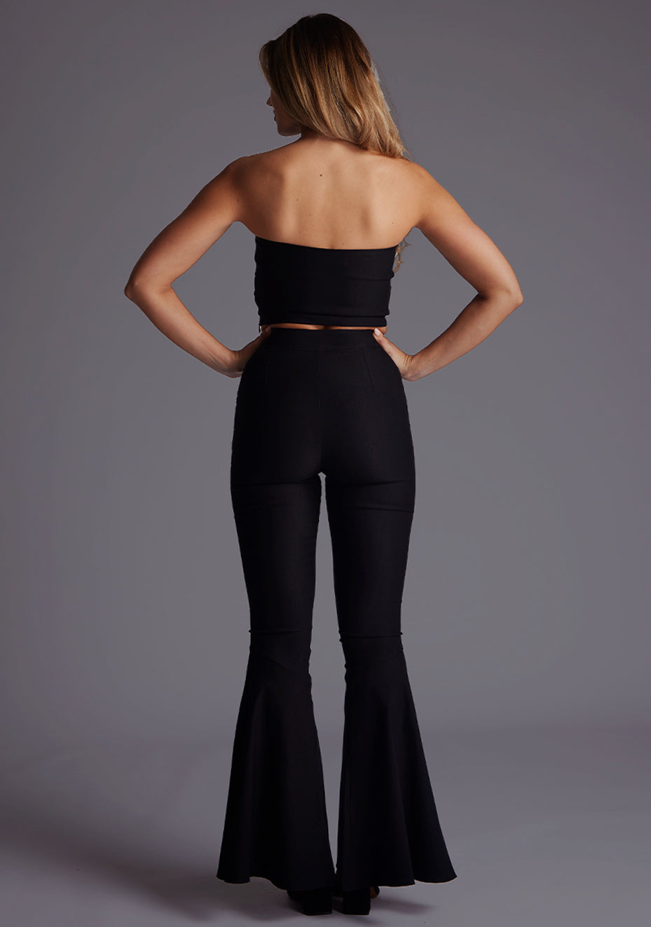 Back image of a model wearing the Vesper Clara High Waisted Flared Trousers in Black, showcasing a sleek high-waisted fit and flowing flared legs.