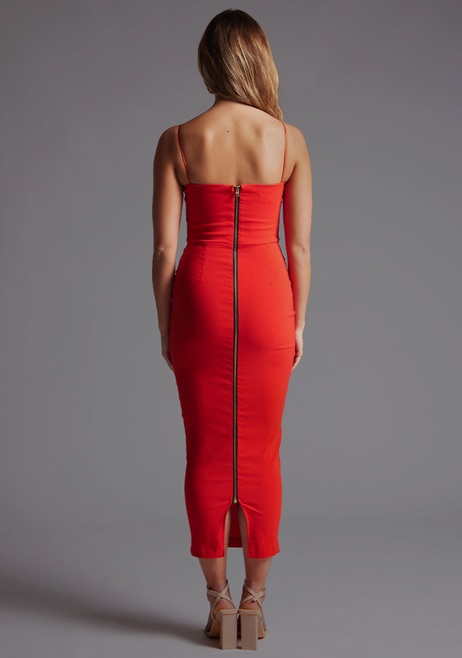 Back image of a blonde model wearing a Red Midaxi Dress with a halter neckline, thin straps, and a front bodice cut-out, the design features the Vesper Jordan Cut-Out Midaxi Dress in Red.