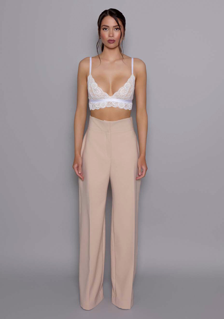 Model wearing the VSPR Lumi High-Waist Tailored Trousers in soft Stone, showing the structured high waist and wide-leg silhouette, standing against a gray studio backdrop.