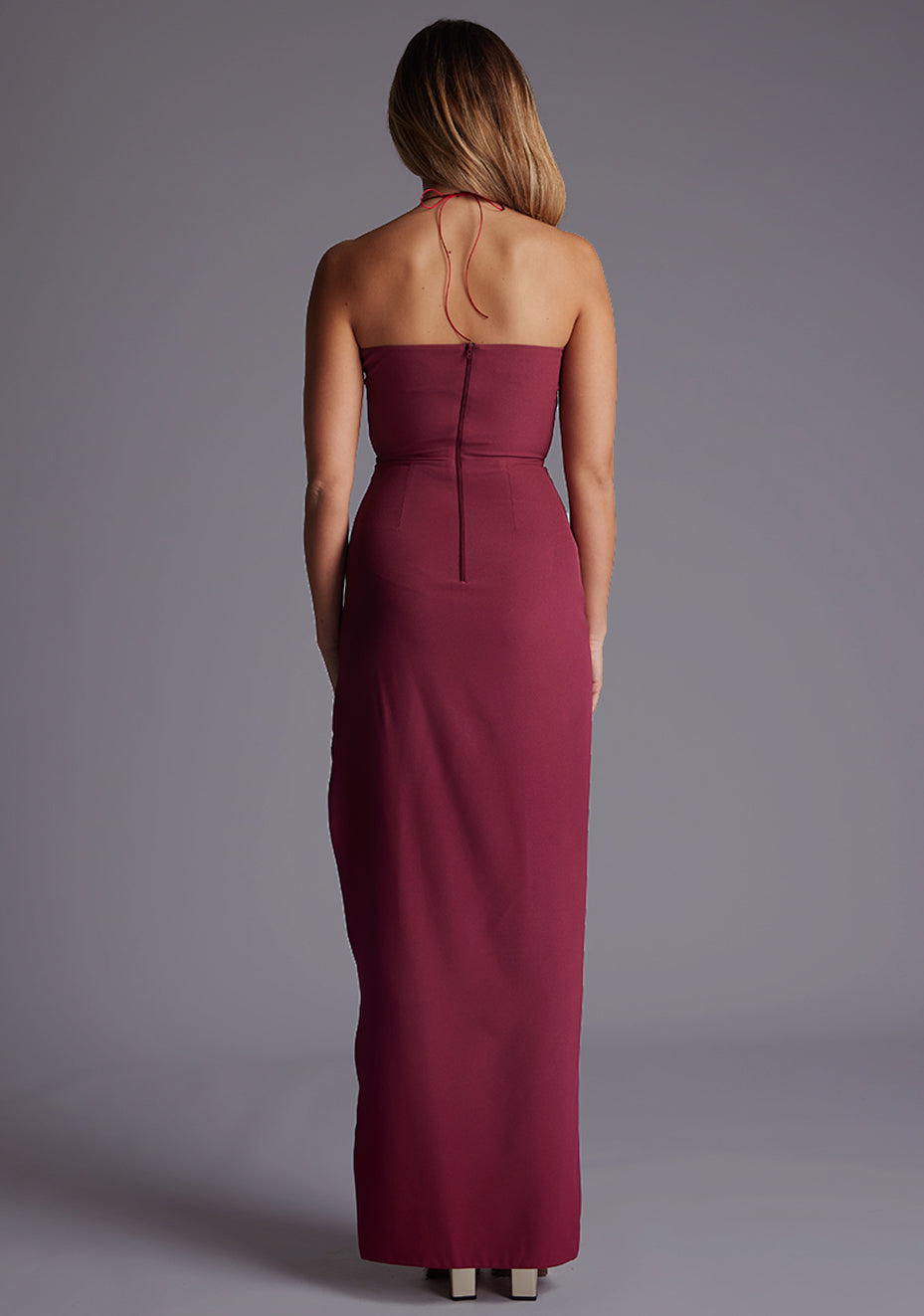 Back image of a model wearing the Vesper Opal Cut-Out Halter Maxi Dress in Burgundy, featuring a clean halter back and fluid maxi skirt