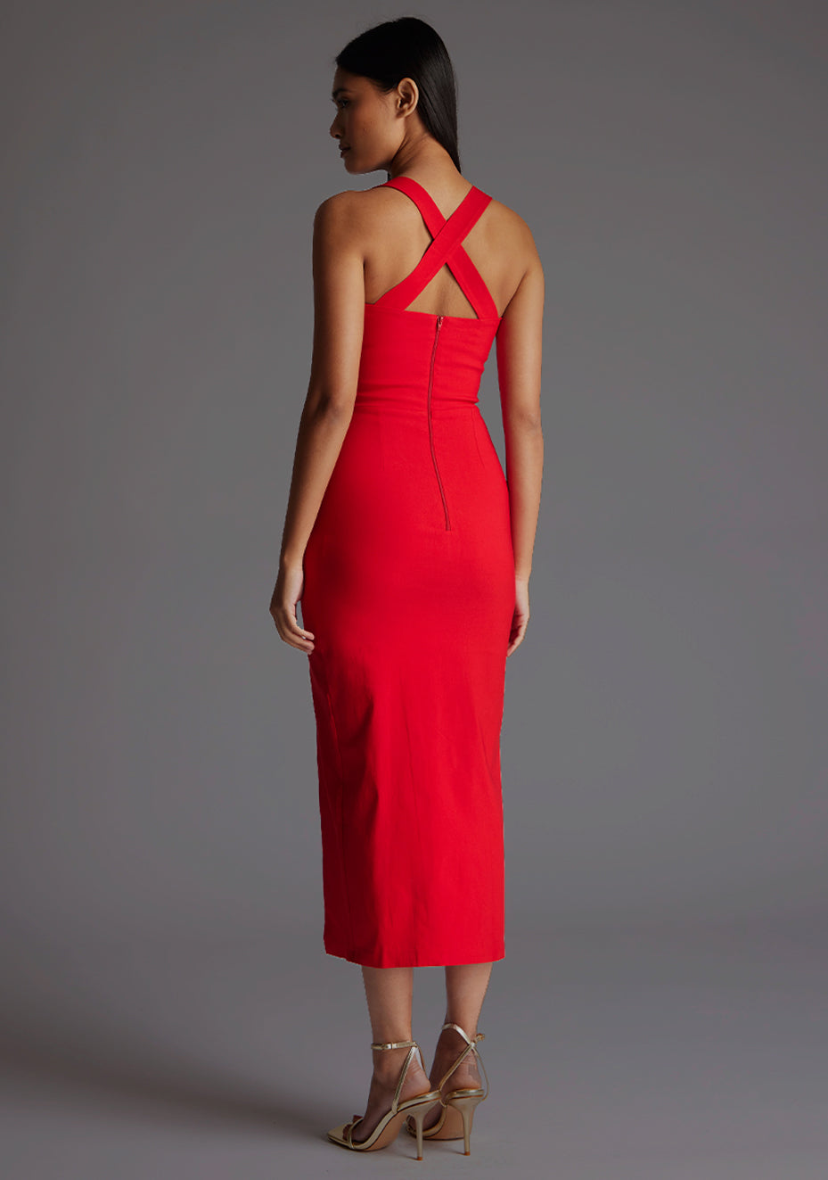 Side back image of a model wearing a red midaxi dress, featuring plunge sweetheart halter neck straps which cross at the back and a front skirt split. The dress featured is the Vesper Poppy Sweetheart Cross Strap Midaxi Dress in Red.