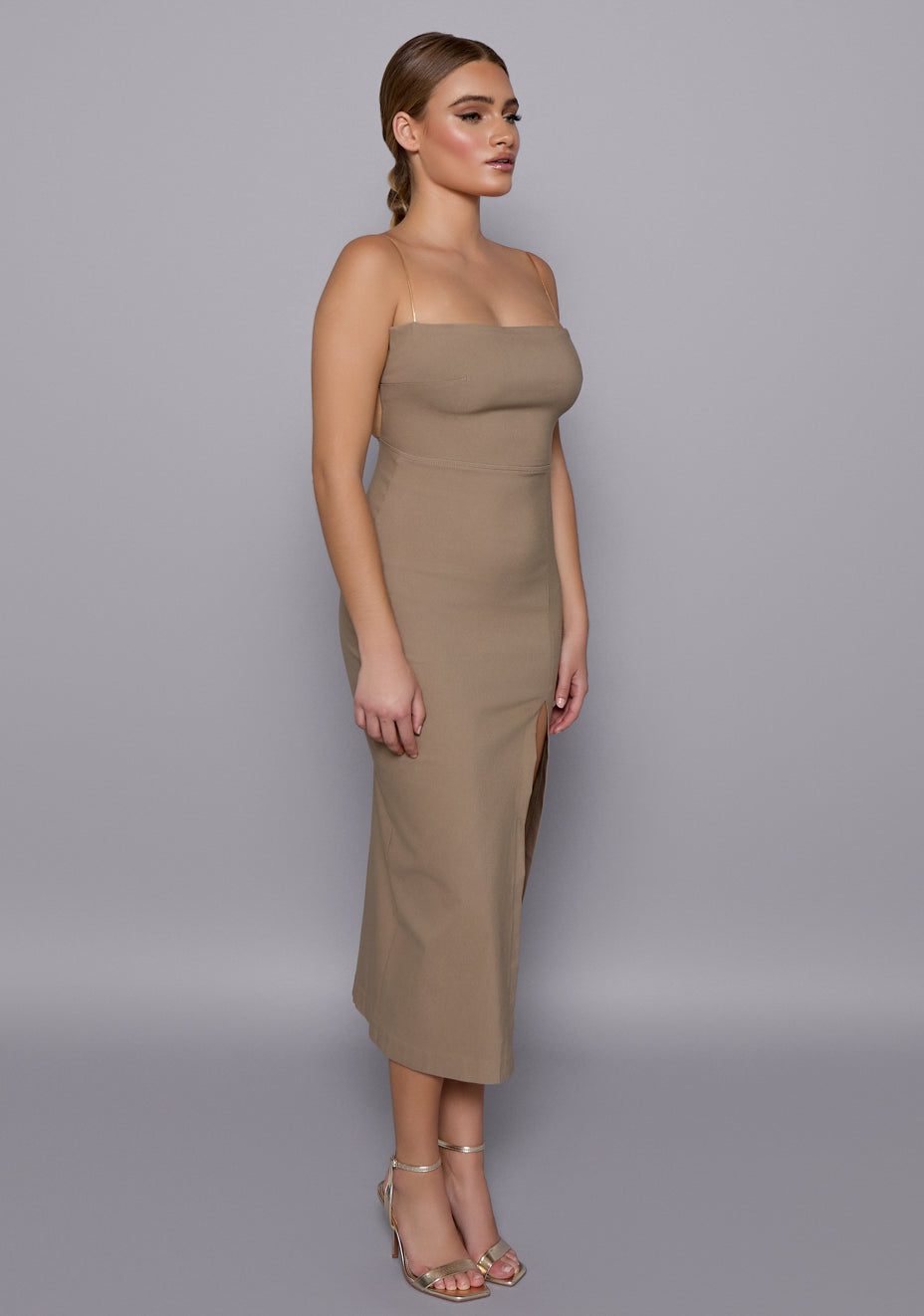 Side-front view of the VSPR Sandra Taupe Midaxi Dress showcasing the body-contouring silhouette, front split, and soft drape of the fabric along the curves.