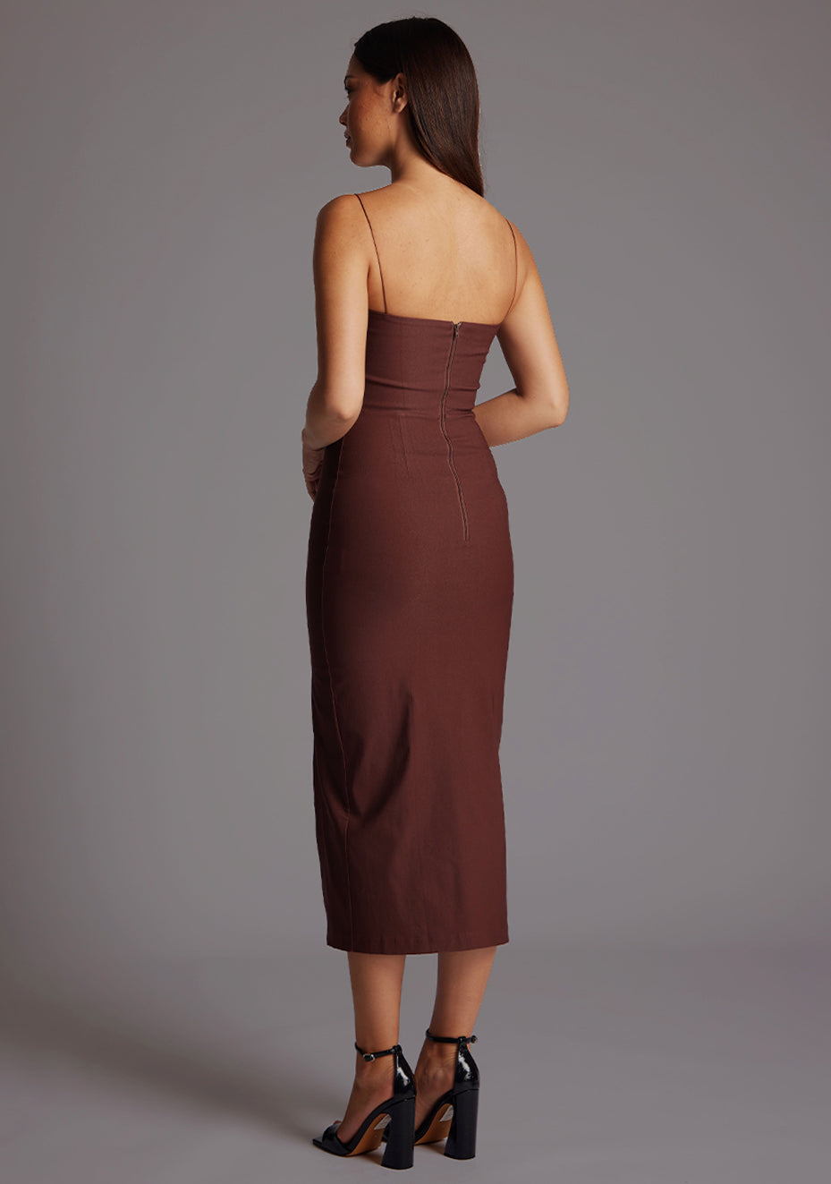 Back quarter image of a model wearing a chocolate midaxi dress with a charming sweetheart neckline, front cut-outs for a sections at the bust and complete with a front skirt split for added movement. The design featured is the Vesper Kendall Chocolate Midaxi Dress