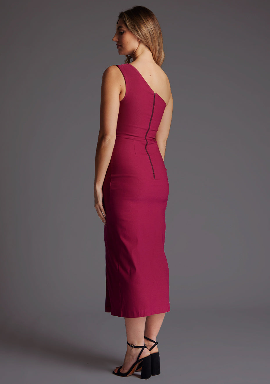 Back quarter image of a model wearing a Marsha Berry One Shoulder Midaxi Dress with a asymmetric neckline, one shoulder detail and front skirt split. The design featured is the Vesper Marsha Berry One shoulder Midaxi Dress.