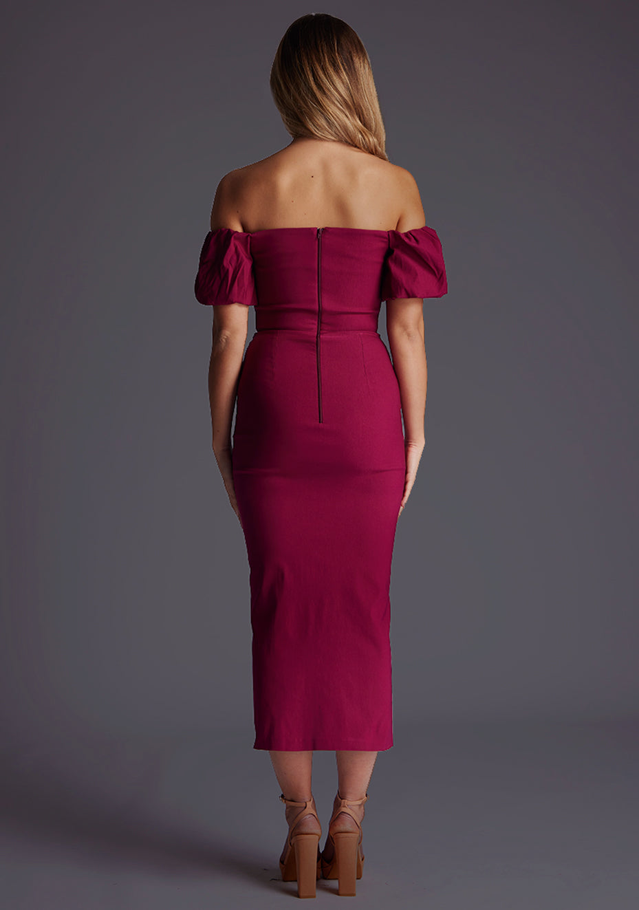 Back image of a blonde model wearing a berry midaxi dress with a bardot neckline gracefully frame off shoulders, while the back zip ensures a seamless silhouette. The design featured is the Vesper Quinton Berry Midaxi Dress.