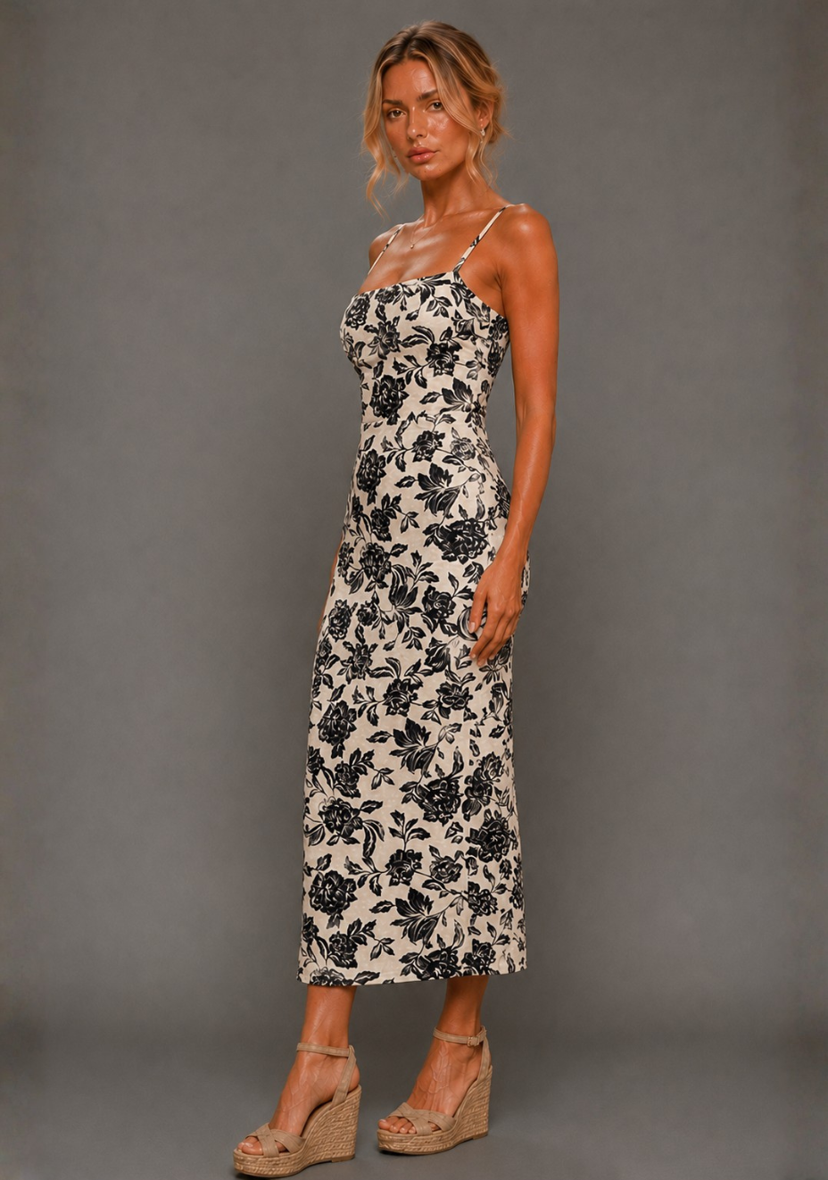 Side front image of a model wearing the VSPR Cora Square Neck Champagne Midaxi Dress, showcasing the contoured bodice, cinched waist, and midaxi length falling gracefully to the floor, standing against a grey studio backdrop.
