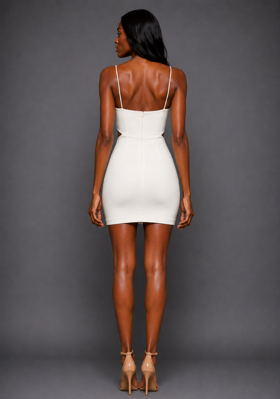Back image of a model wearing the VSPR Fiona Strappy Bodycon Ivory Mini Dress featuring fine shoulder straps, a smooth fitted silhouette and mini-length hem, standing against a grey studio backdrop.