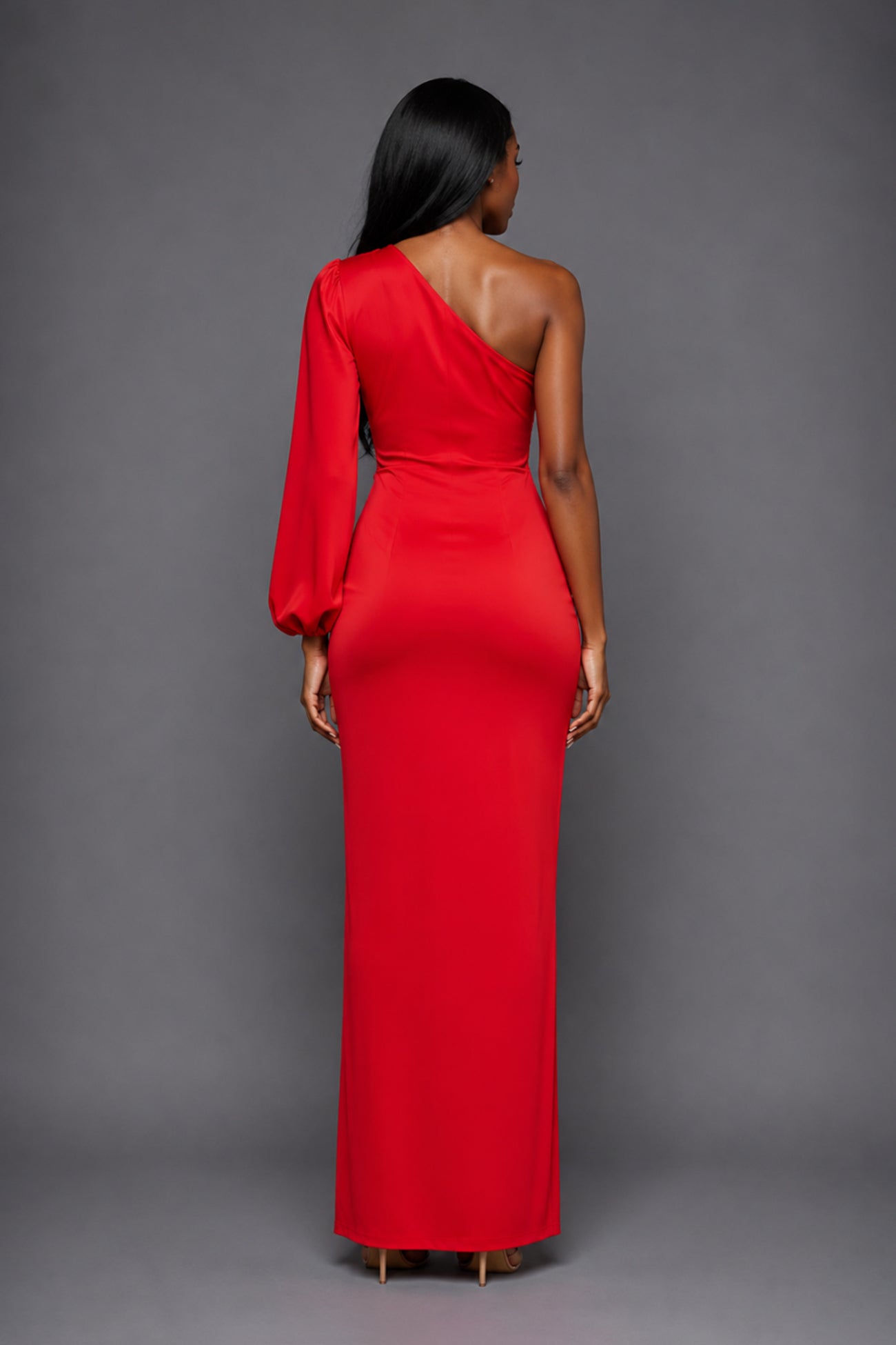 Back image of a model wearing the VSPR Keaton One Sleeve Red Maxi Dress, showcasing its elegant floor-length silhouette and refined drape against a grey studio backdrop.