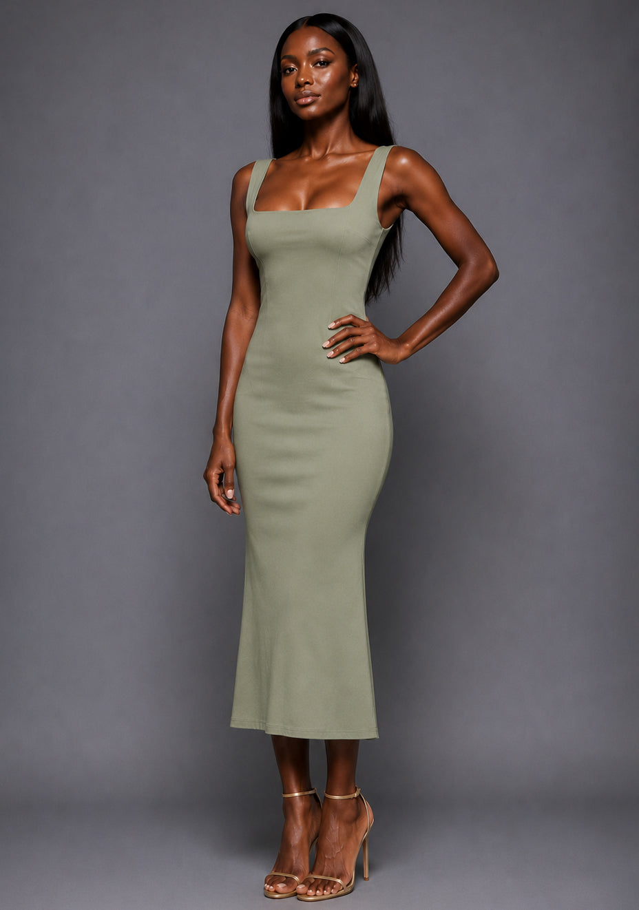 Side-front image of a model wearing the VSPR Marianna Square Neckline Fishtail Olive Midaxi Dress, highlighting the fitted waistline and softly flared fishtail hem against a grey studio backdrop.