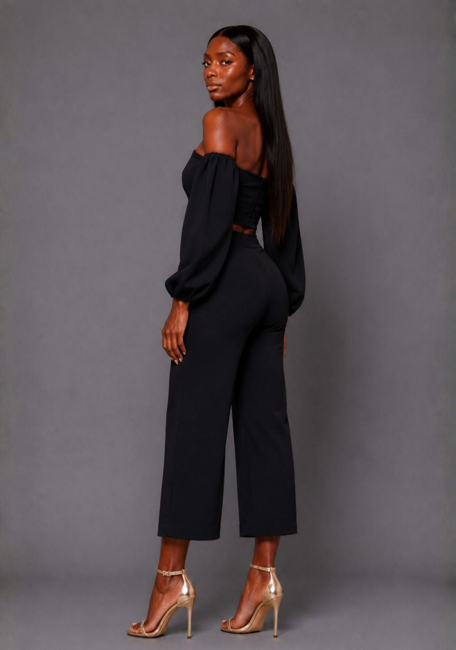 Side front image of a model wearing the VSPR Mindi Wide Leg Black Cropped Trousers, highlighting the high-rise fit and fluid wide-leg silhouette against a grey studio backdrop.