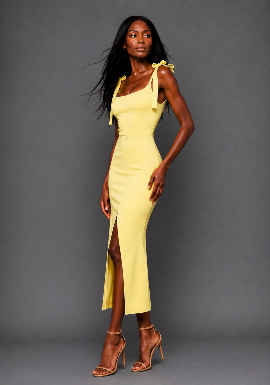 Side front image of a model wearing the VSPR Onyx Square Neck Bow Lemon Midaxi Dress on a model, showcasing the sculpted shape, vibrant lemon hue, square neckline, and graceful skirt split against a grey studio backdrop.