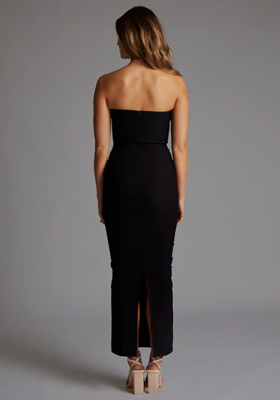 Back image of a model wearing the Vesper Calix Bandeau Maxi Dress in Navy, emphasizing the strapless finish and elegant maxi-length flow.