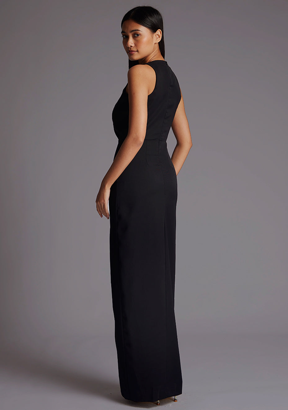 Side back image of a model wearing a black sleeveless maxi dress with   sleeveless design and flattering V-neckline accentuates your figure while the body con fit gracefully hugs your curves. The design featured is the Vesper Elba V-neckline Maxi Dress in Black.