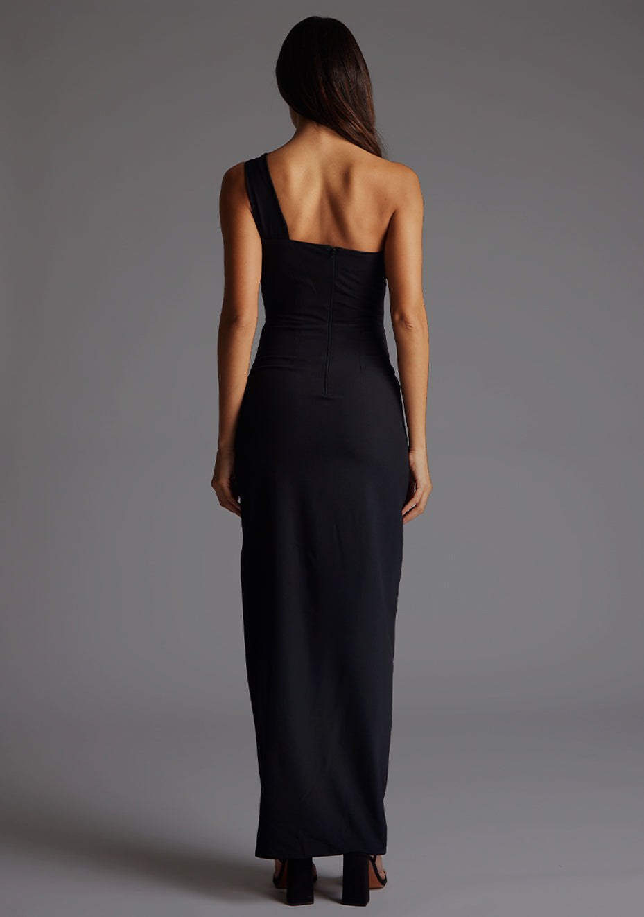 Back image of the model wearing a black maxi dress with a sleek one-shoulder silhouette, contemporary front cut-out and front skirt split for effortless chic.  The design features Vesper Ellis Cut-Out One-Shoulder Maxi Dress in Black.