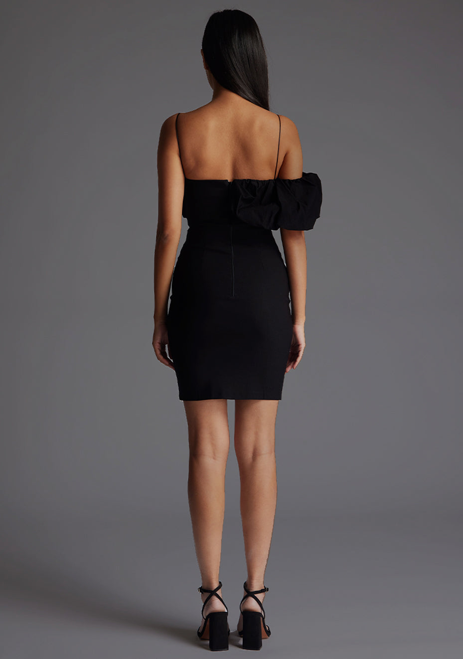 Back image of a model wearing a Black Mini Dress with a square neckline with thin straps that enhance your shoulders and a flattering puff design that adds a touch of femininity, The dress featured is the Vesper Hattie Cami Strap Mini Dress in Black.