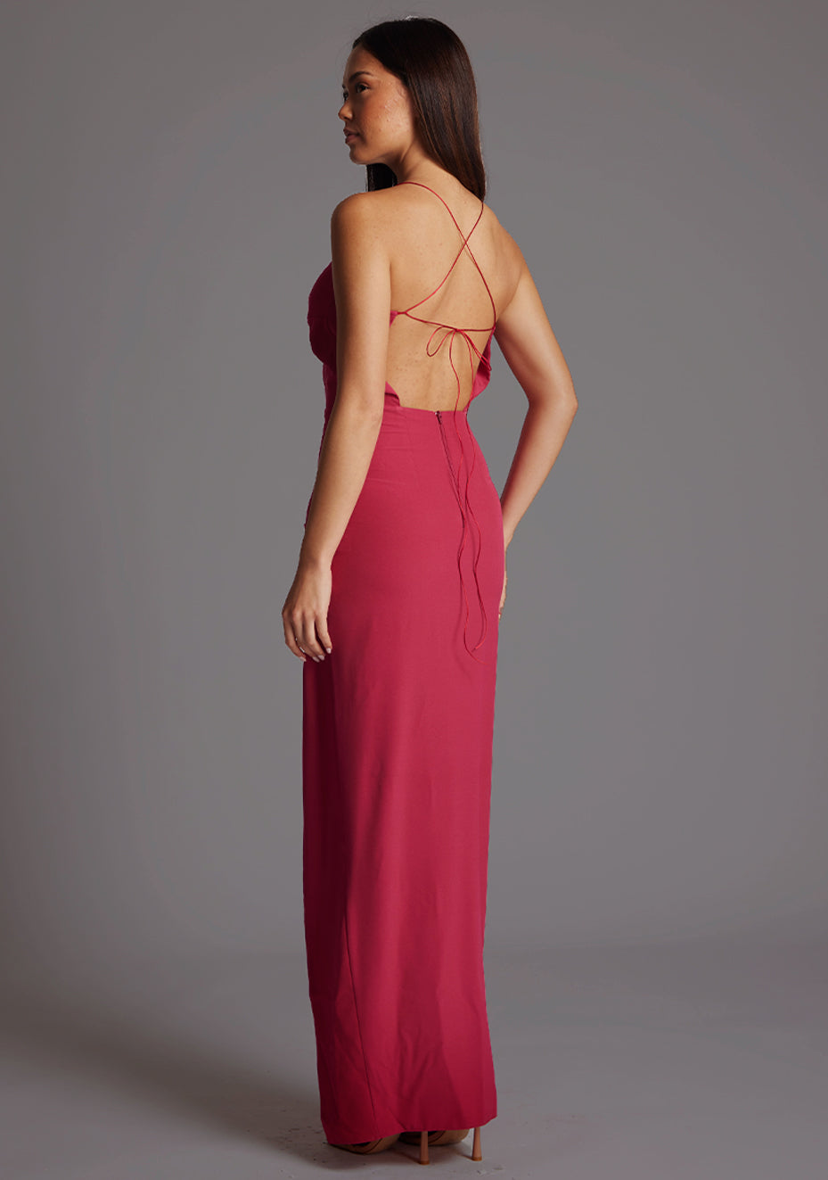 Side back image of a model wearing the Vesper Maggie Sweetheart Neckline Maxi Dress in Raspberry, revealing the delicate criss-cross tie back detail and flowing skirt.