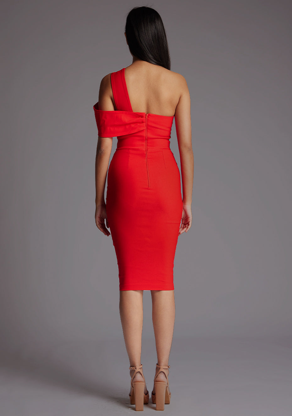 Back image of a model wearing a red midi dress with a eye-catching asymmetric and one-shoulder dress, front cut-out adds a touch of allure and while the bodycon fit accentuates your curves flawlessly. The design featured is the Vesper Novi Asymmetric One Shoulder Midi Dress in Red.