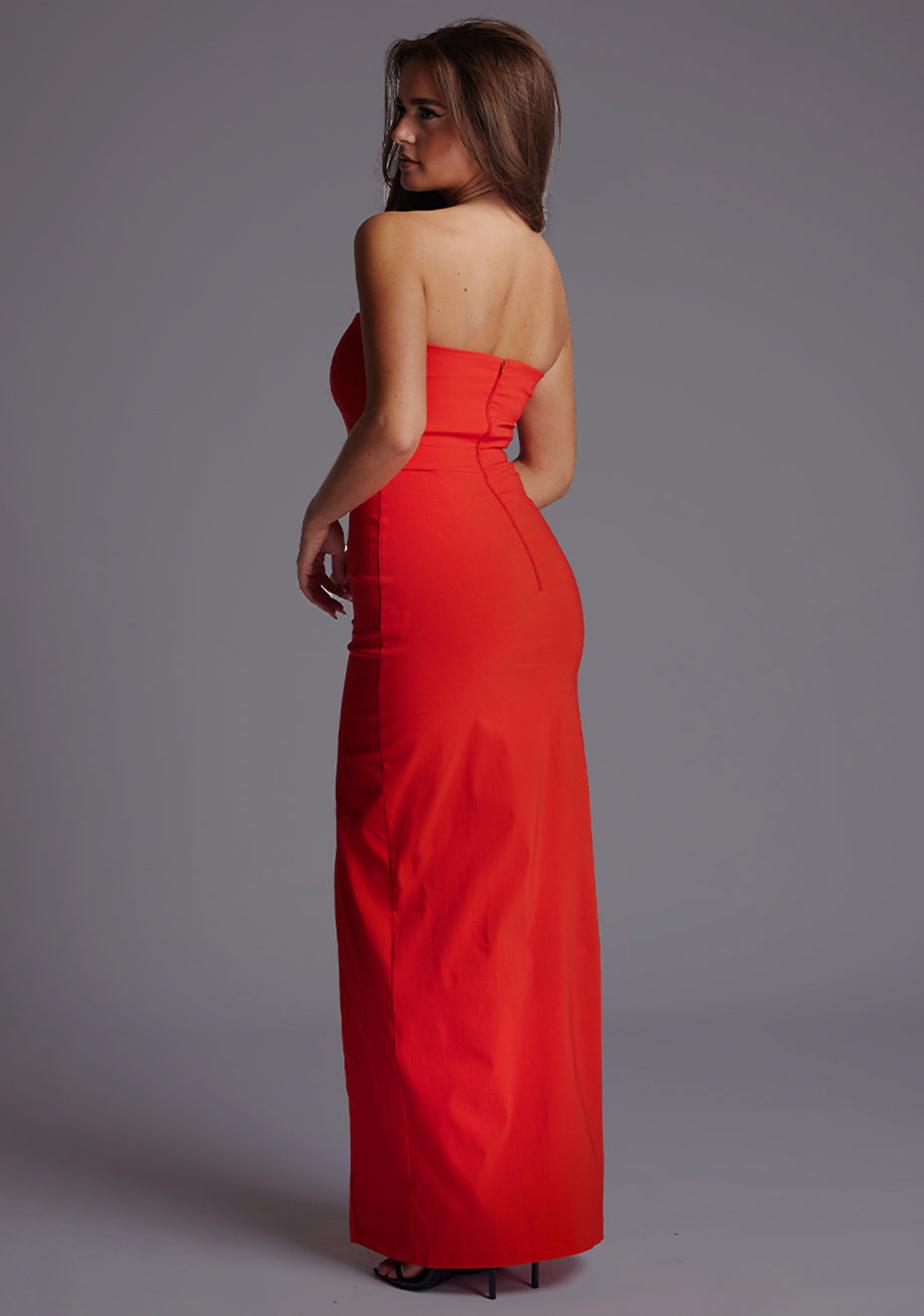 Side back image of a model wearing the Vesper Salma Bandeau Thigh Split Maxi Dress in Red, showcasing the smooth strapless back and streamlined fit.