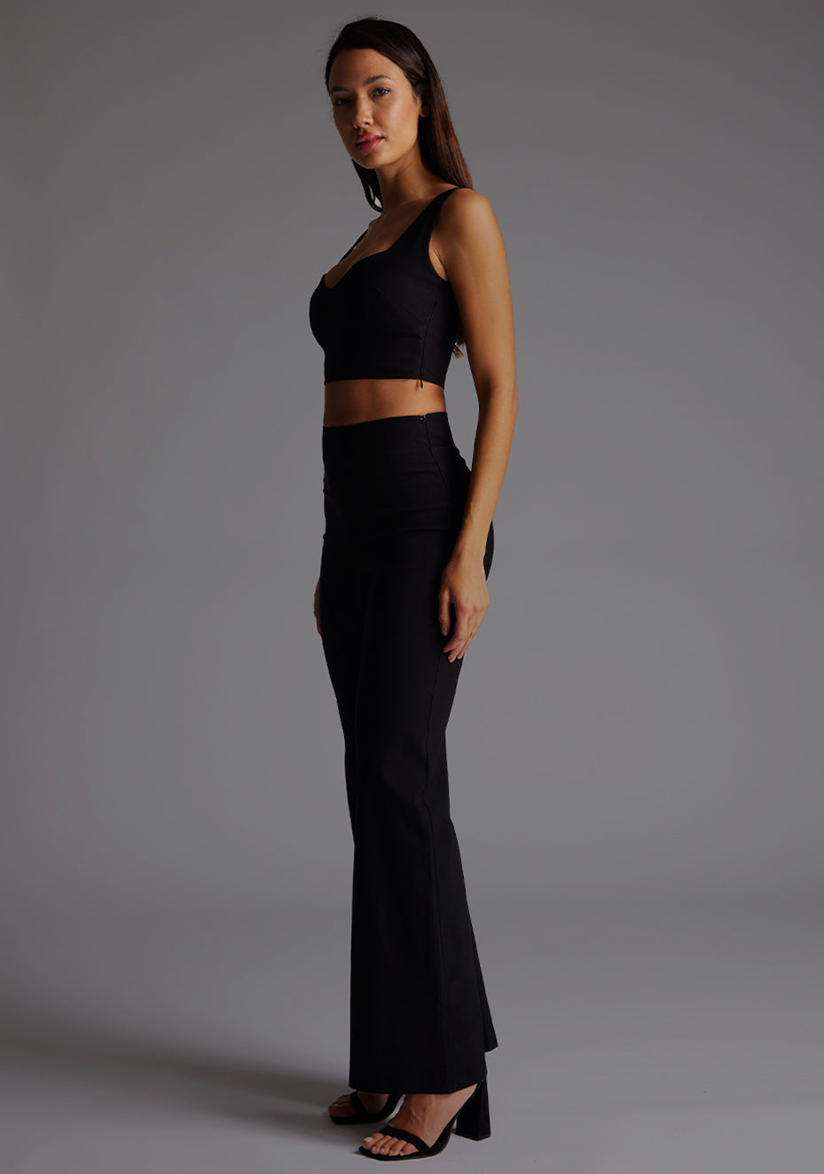 Side front image of a model wearing a black crop top with a sweetheart neckline and thick straps. The design featured is the Vesper Sweetheart Neckline Crop Top in Black pair with Vesper June Wide Leg Trousers in Black.