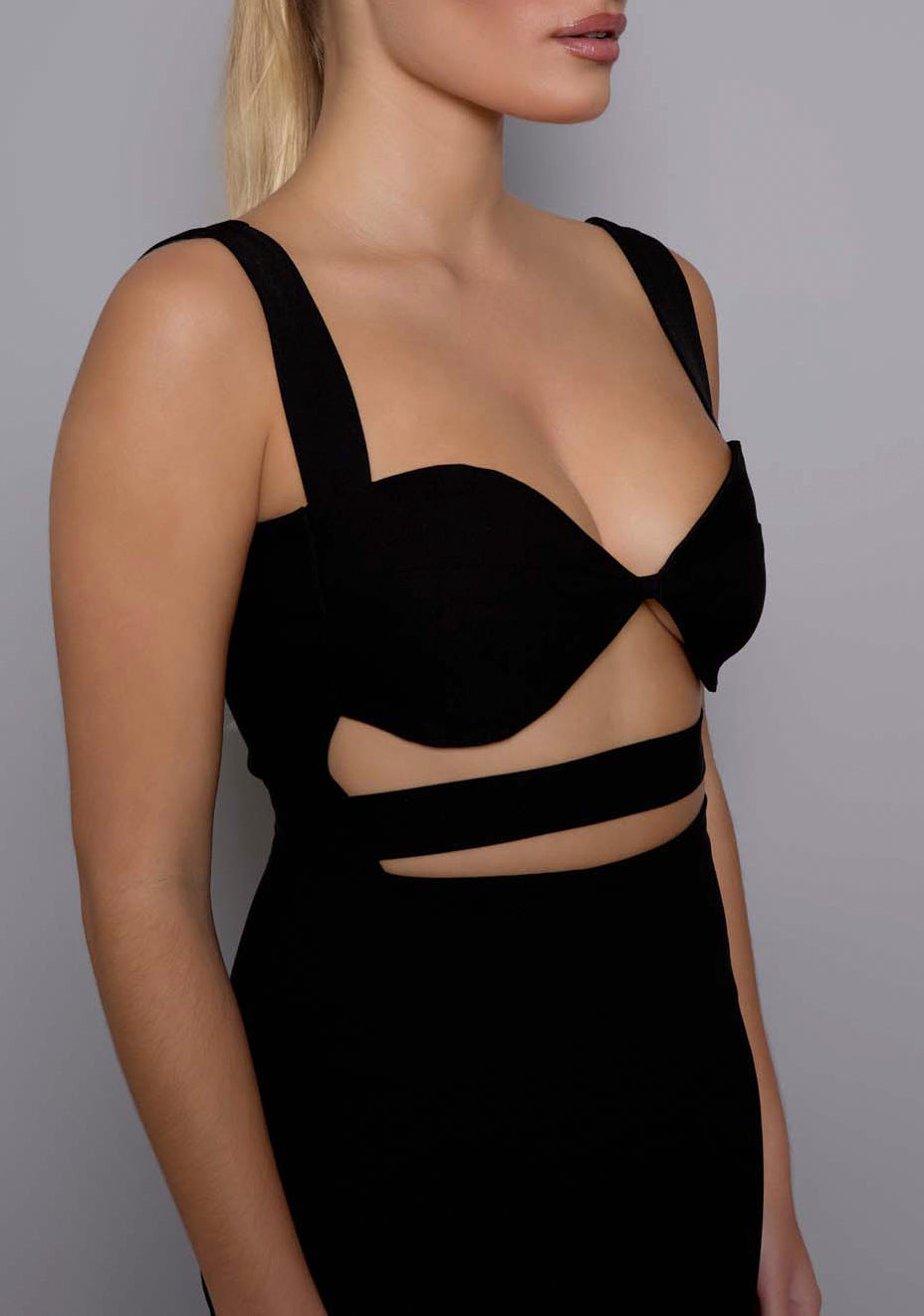 Close-up side front view of the VSPR Solene black dress, focusing on the bold under-bust cut-outs, wide straps, and smooth premium fabric that shapes the silhouette.