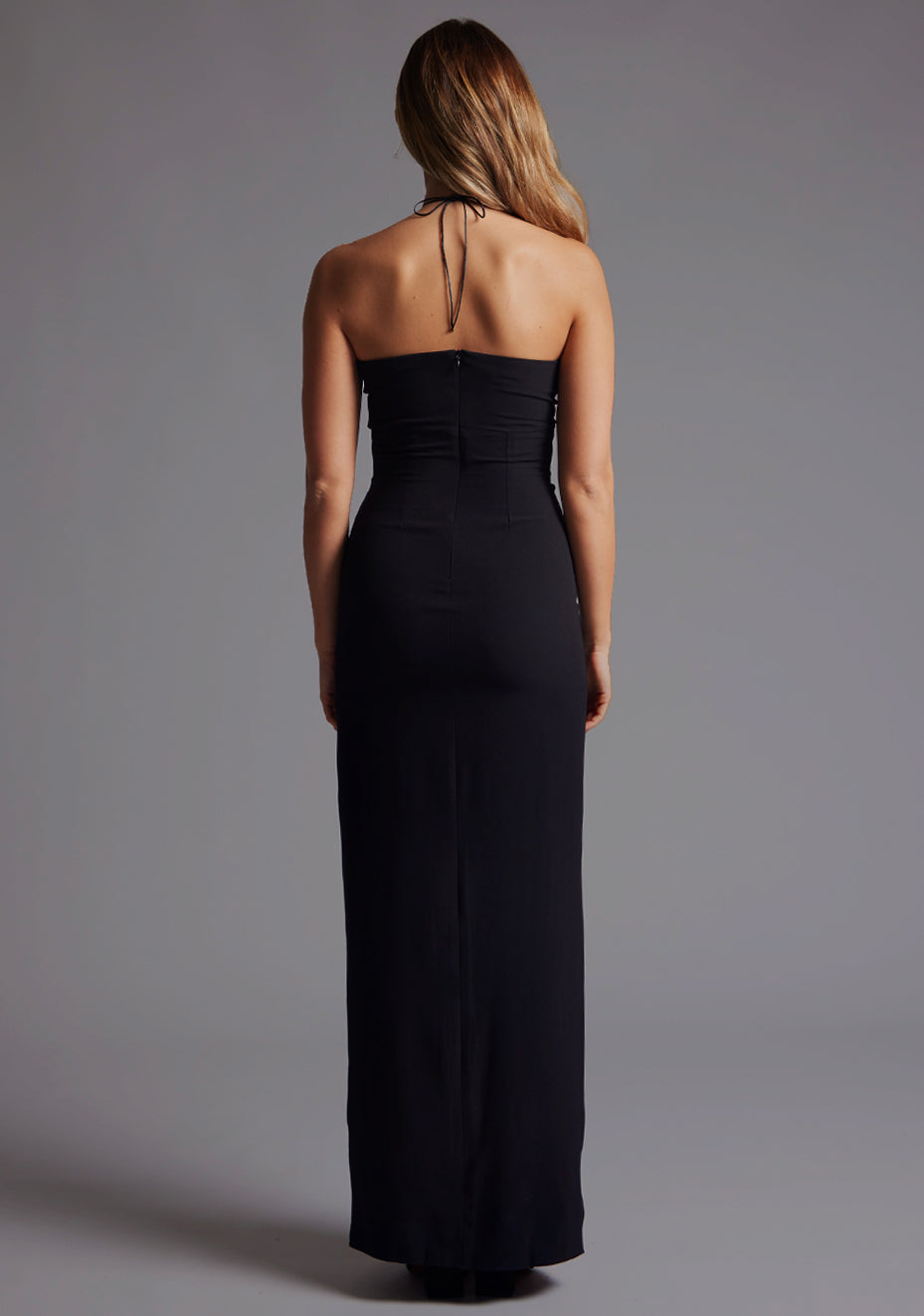 Back image of a model wearing the Vesper Tanya Halter Neck Maxi Dress in Black, featuring a sleek open-back halter design and flowing maxi length.
