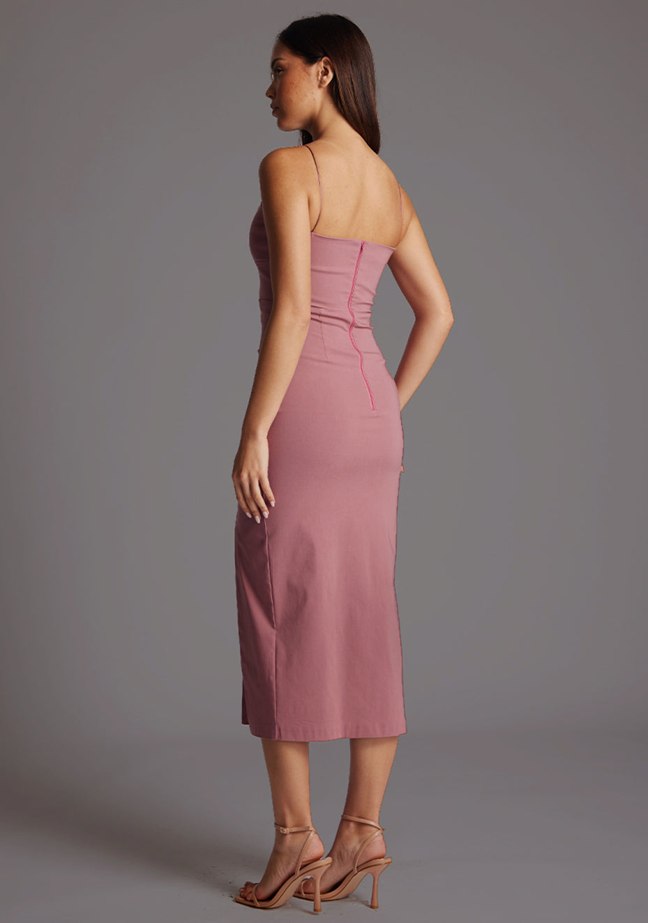 Back quarter image of a model wearing a rose midaxi dress with a plunging neckline with thin straps, a front bodice cut-out and front skirt split. The design featured is the Vesper Martina Rose Midaxi Dress