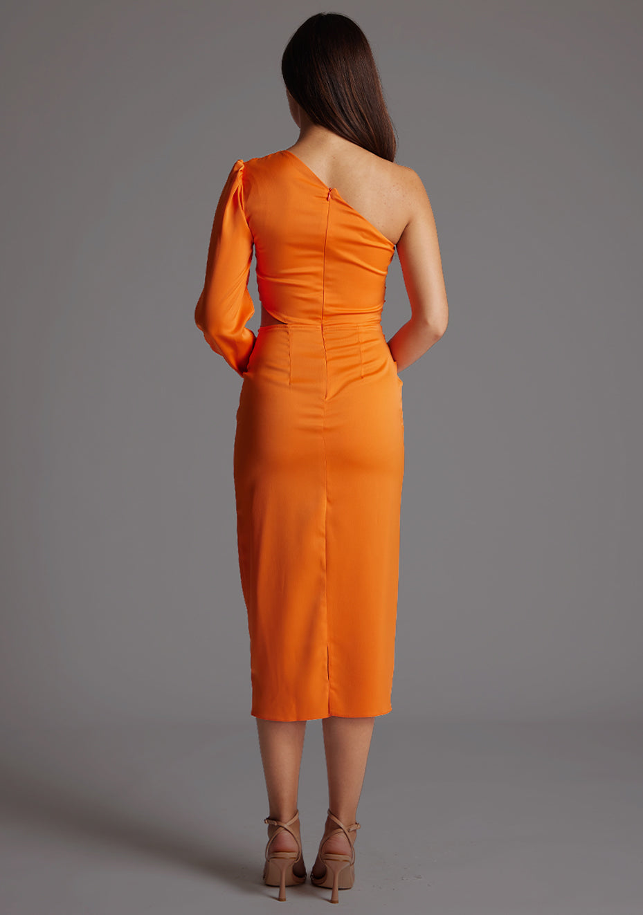 Back image of a model wearing an orange mid dress with a asymmetric, one long sleeve design and subtle side cut-out.  The design featured is the Vesper Niccola Orange Midi Dress