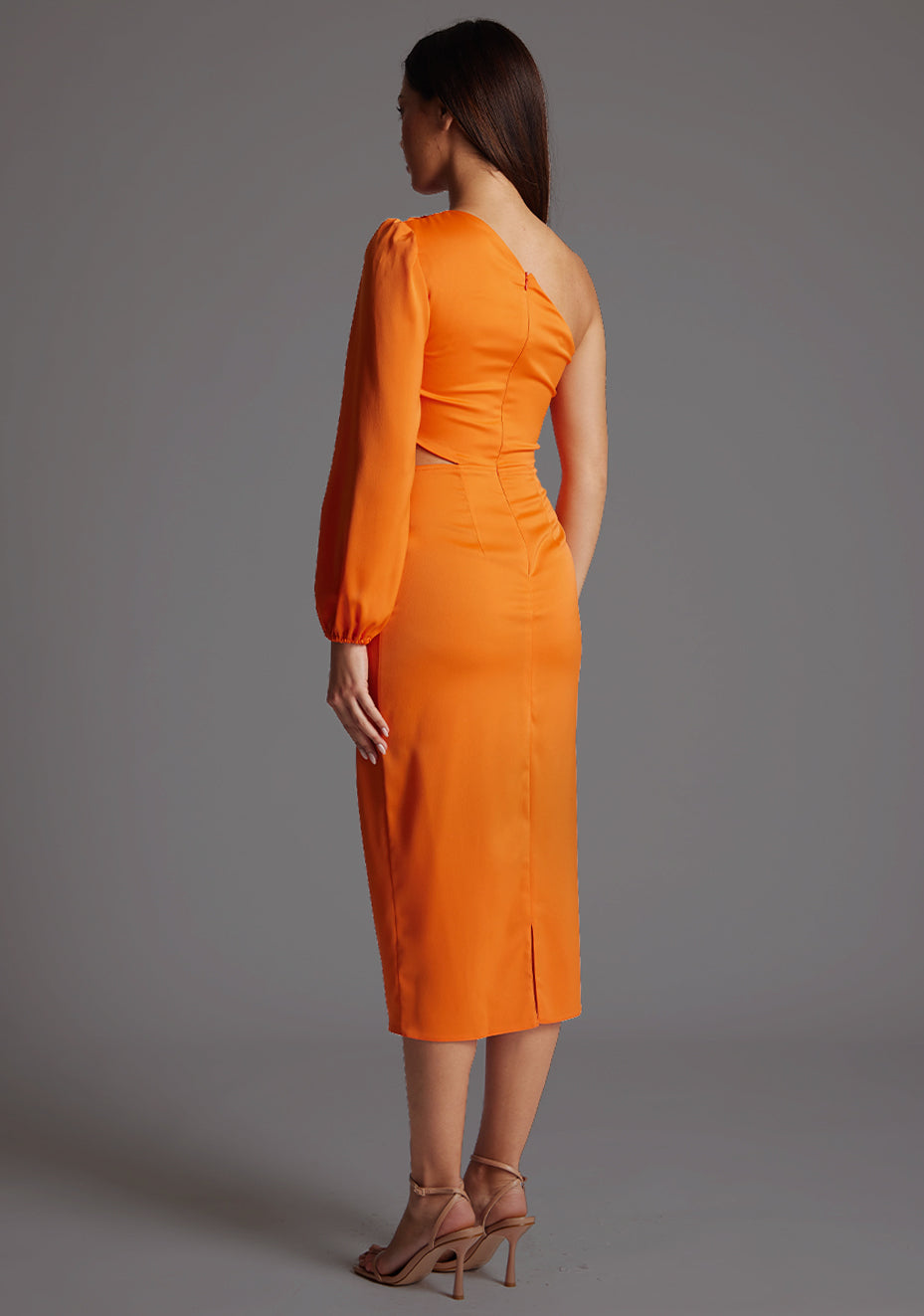 Back quarter image of a model wearing an orange mid dress with a asymmetric, one long sleeve design and subtle side cut-out.  The design featured is the Vesper Niccola Orange Midi Dress