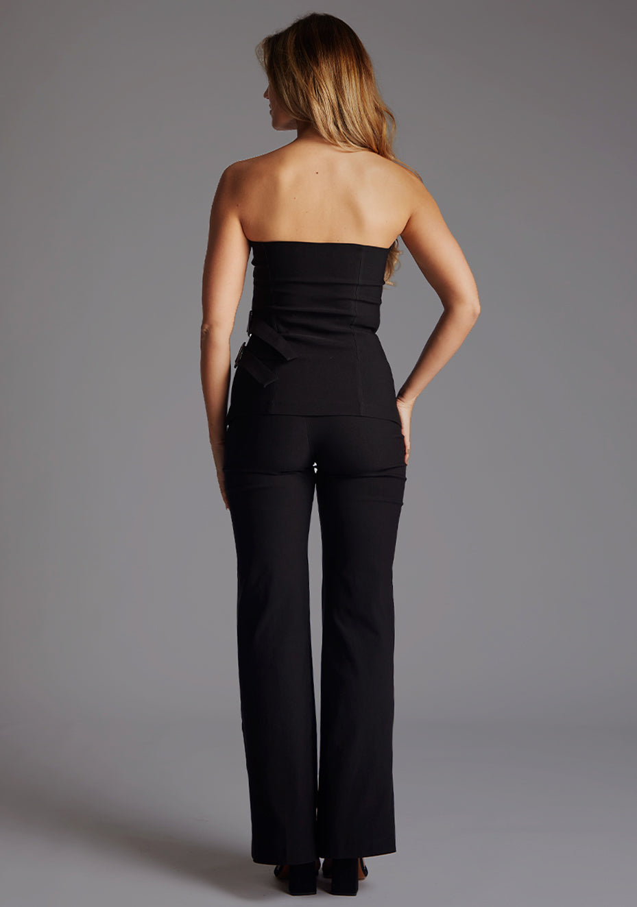 Back image of a model wearing a strapless black to with a  chic strapless design with modern buckle detail. The design  featured is the Vesper Sharon black Top paired with the Vesper June Black Wide Leg Trousers