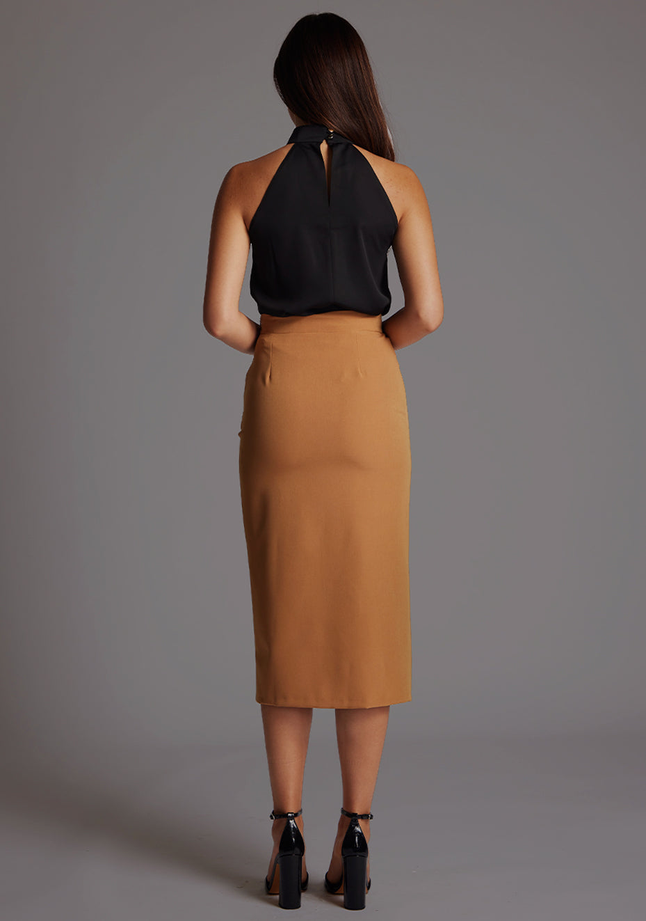 Back image of a model wearing the Vesper Sherine High Waist Pencil Skirt in Camel, showcasing the streamlined back silhouette.