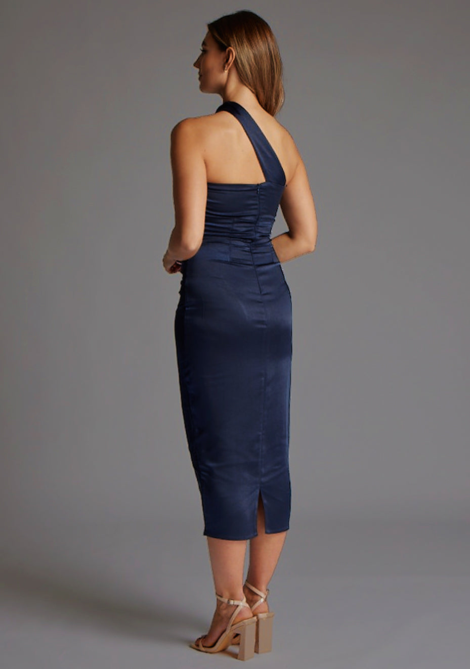 Back quarter image of a model wearing a navy midaxi dress with a asymmetrical neckline, one-shoulder design and shirred bust with cut-out detail adds a touch of sophistication. The design featured is the Vesper Tierney Navy Midaxi Dress