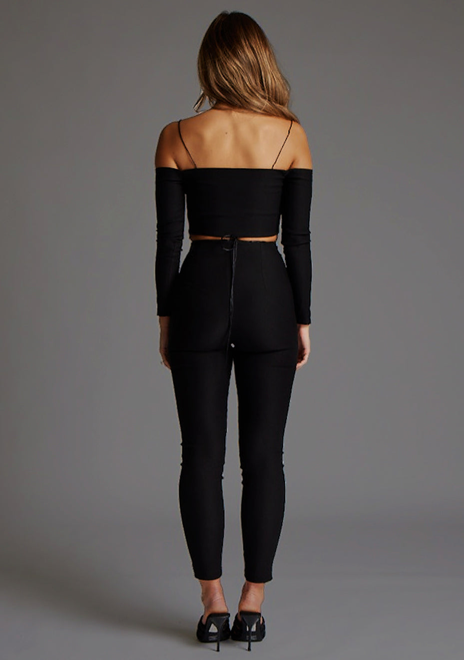 Back image of model wearing a black top with a alluring thin straps, off-shoulder long sleeves and a front criss-cross. The design featured is the Vesper Valeria Black Top pair with Vesper Mila Black Trouser