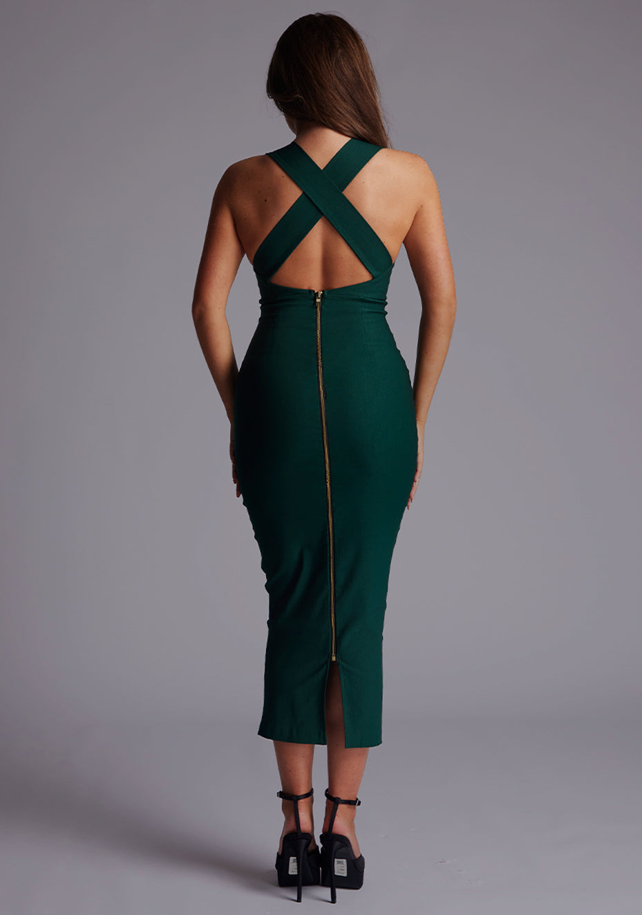 Back image of a model wearing a forest green midaxi dress with a stunning sleeveless masterpiece, plunging v-neckline ,slim silhouette and cross back and gold zip at the back. The design featured is the Vesper Verona Forest Green Midaxi Dress