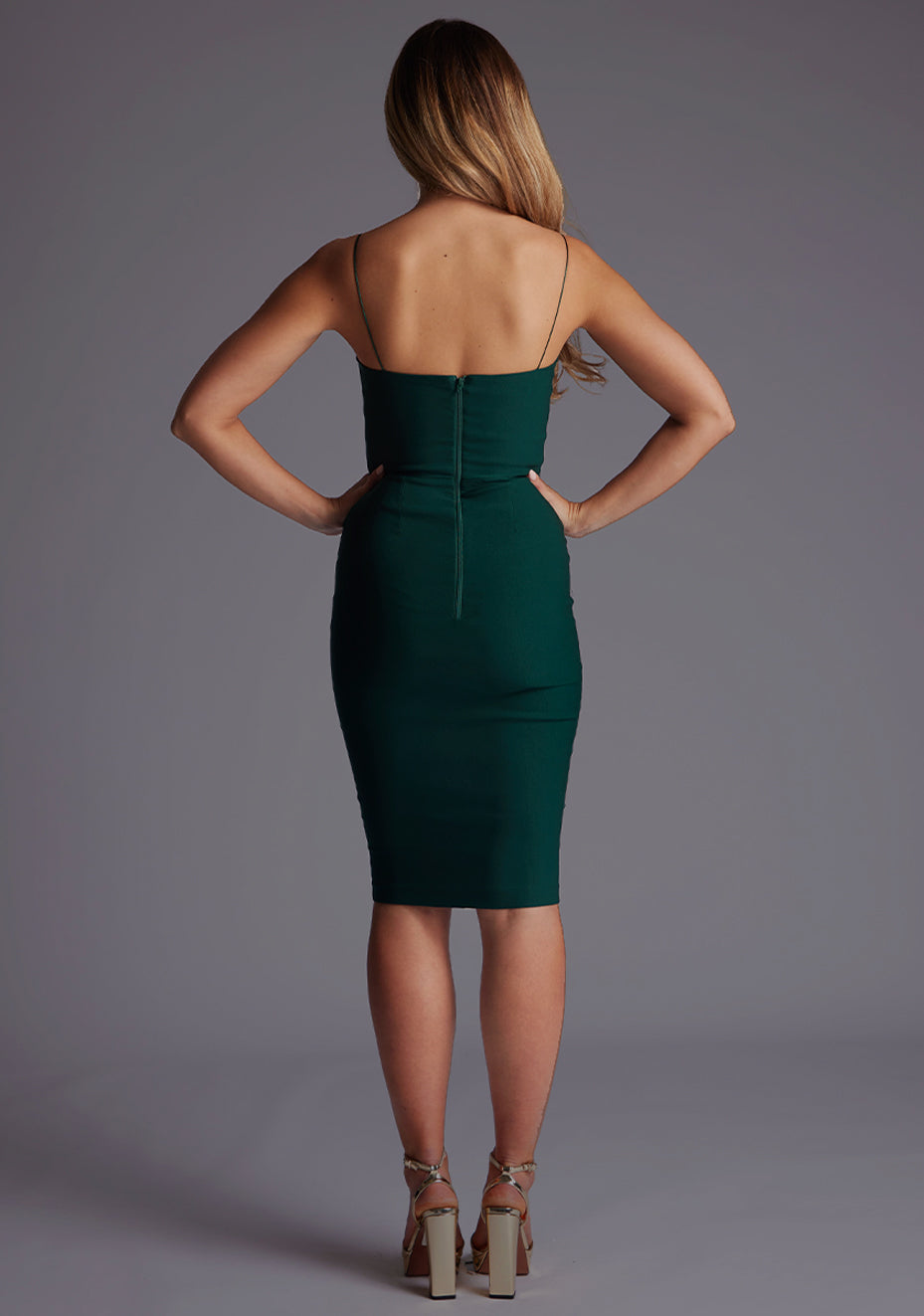 Back image of a model wearing a forest green midi dress with a delicate stylish thin straps, front cut outs with modern twist, bodycon fit and invisible centre back zip. The design featured is the Vesper Zahra Forest Green Midi Dress.