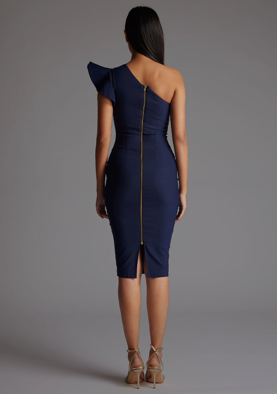 Back image of a model wearing a  navy one shoulder midi dress with a stunning one-shoulder design with ruffle detail and an asymmetric neckline, all tied together with a gold centre back zip. The design featured is the Vesper Zanab Navy One Shoulder Midi Dress.