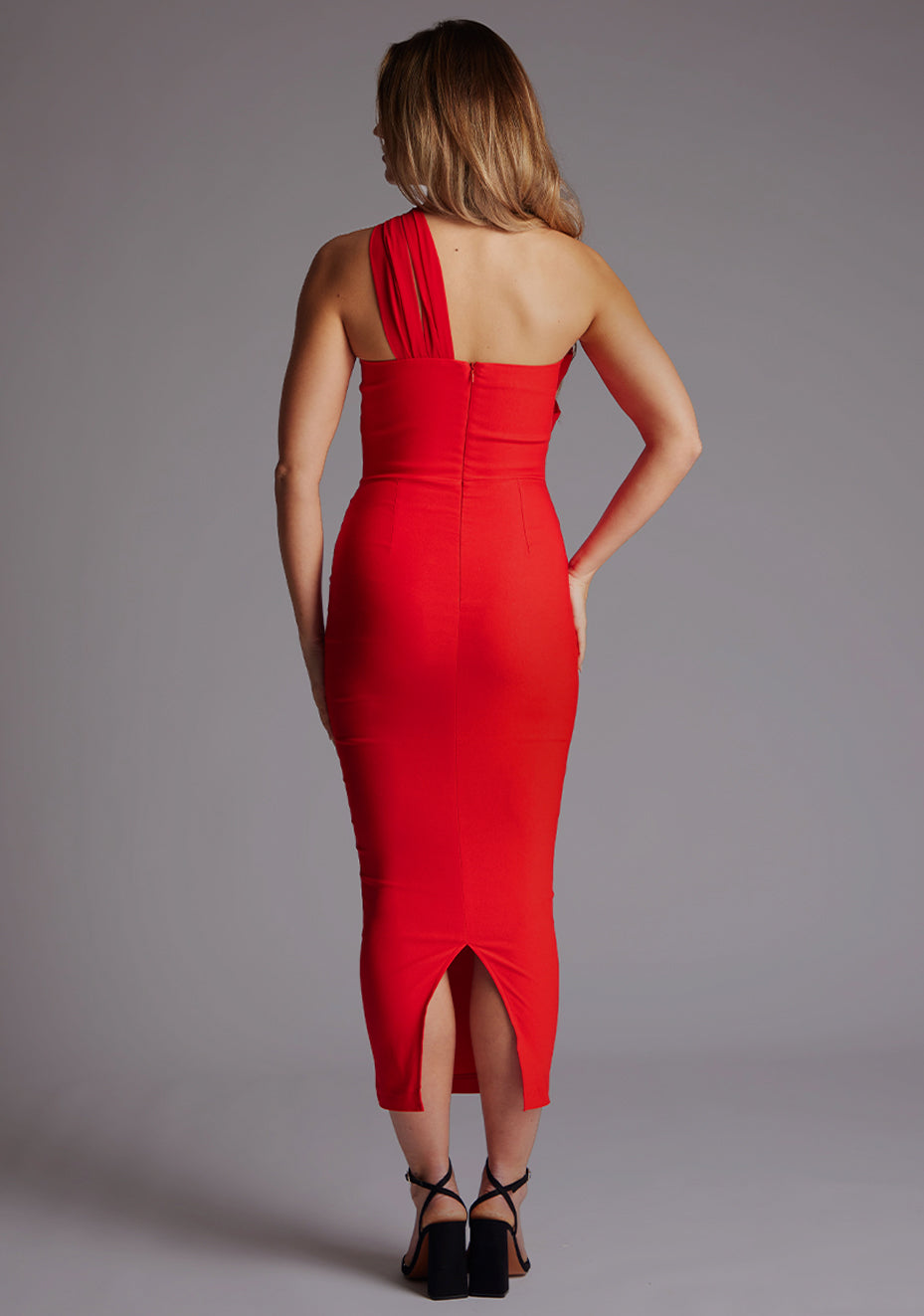 Back image of a model wearing a red midaxi dress with a straight neckline, asymmetric strap across chest with chic cut-out double strap, bodycon fit and invisible centre back zip. The design featured is the Vesper Zenobia Red Midaxi Dress
