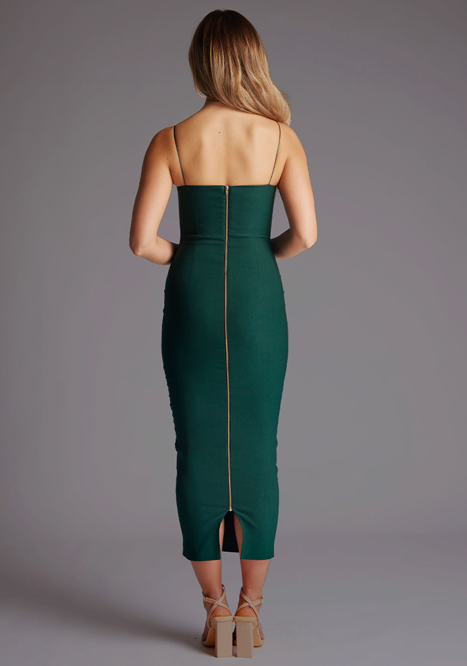 Back image of a model wearing a forest green midaxi dress with a flattering scoop neckline embellished with delicate thin straps, and a subtle front cut-out that imparts a sense of refined allure and statement centre gold back zip. The design featured is the Vesper Zendeya Forest Green Midaxi Dress.